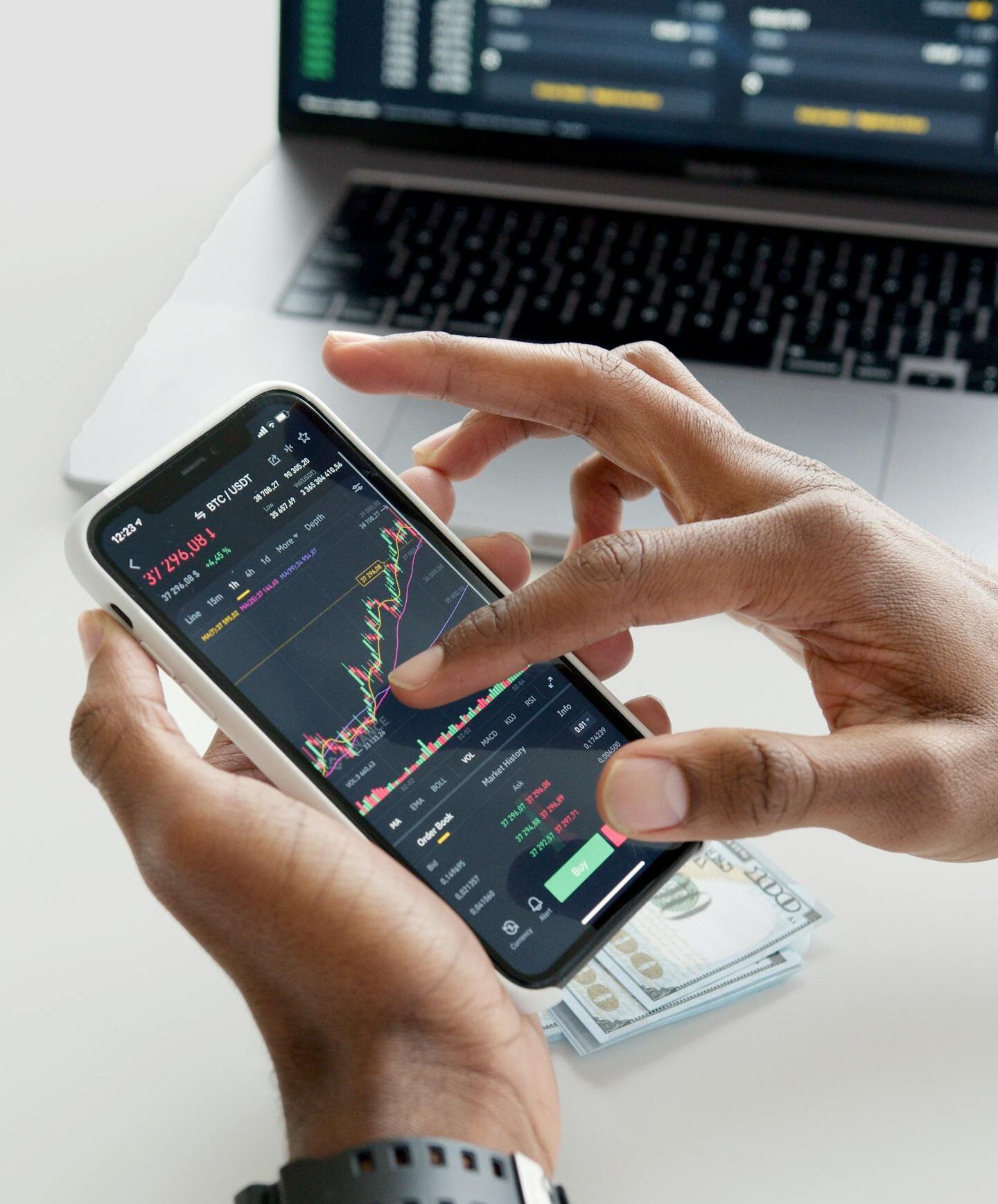 Hands using smartphone trading app with charts, dollar bills in background.